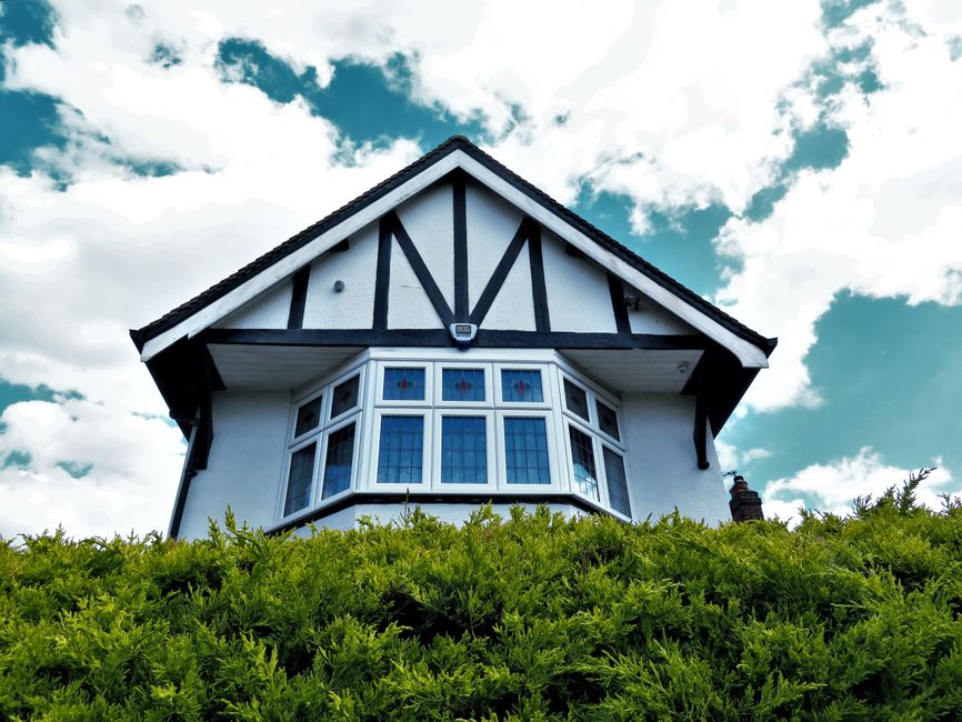 Tudor-style house facade with a bay window against a vibrant sky and greenery.