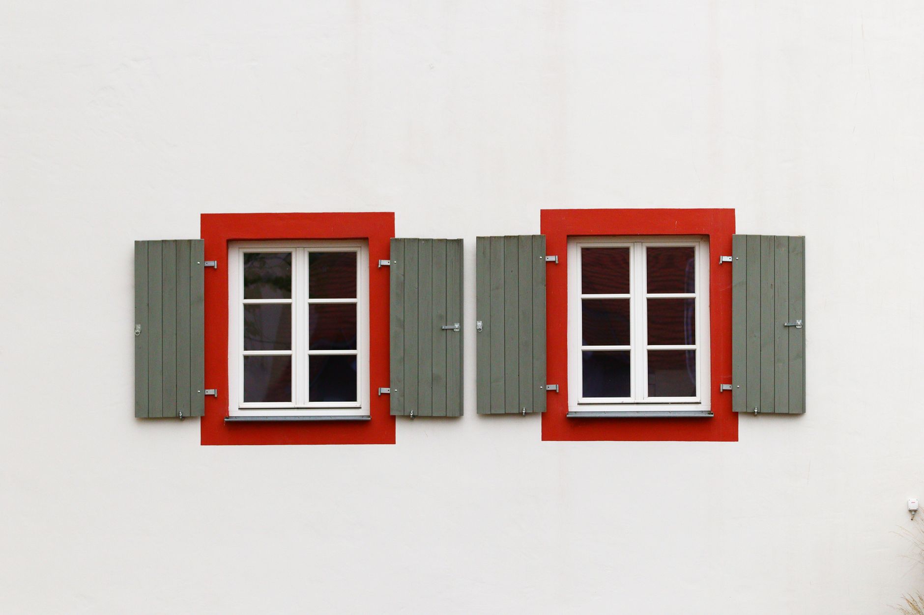 Two red framed windows with green shutters on a minimalist white wall. Architectural detail in Austin, TX